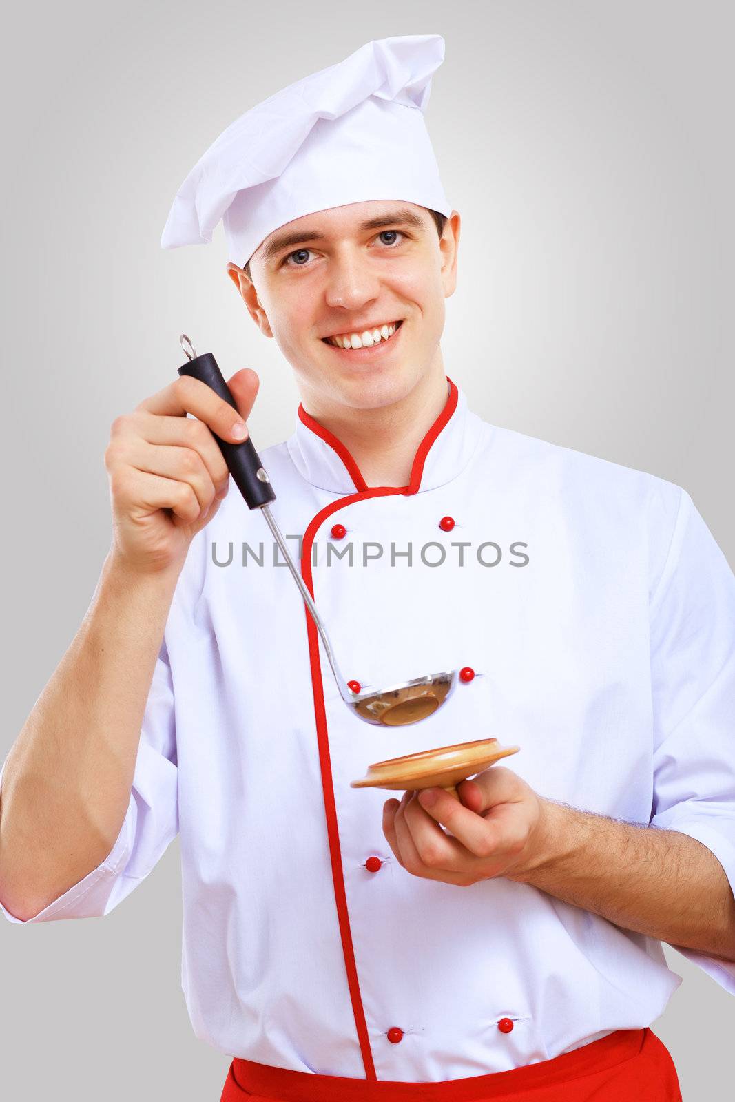 Young male chef in red apron against grey background