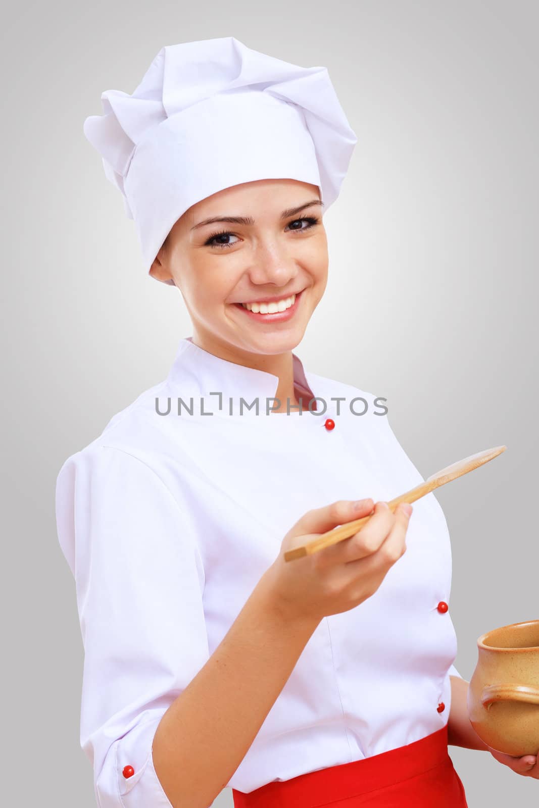 Young female chef in red apron against grey background