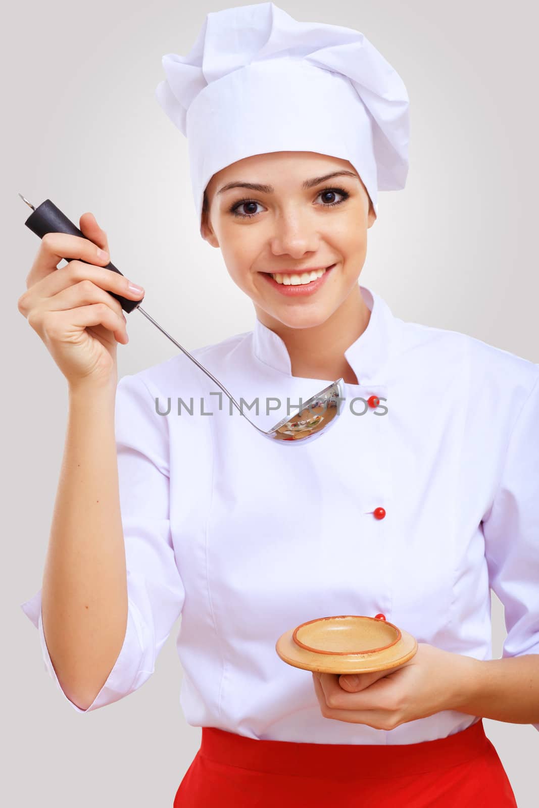 Young female chef in red apron against grey background