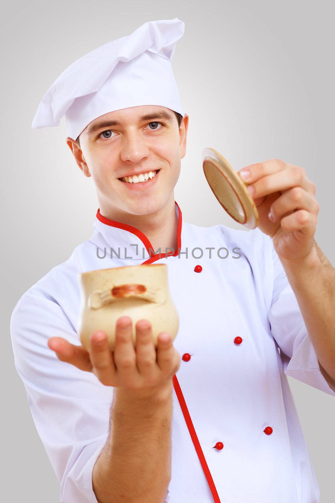 Young male chef in red apron against grey background