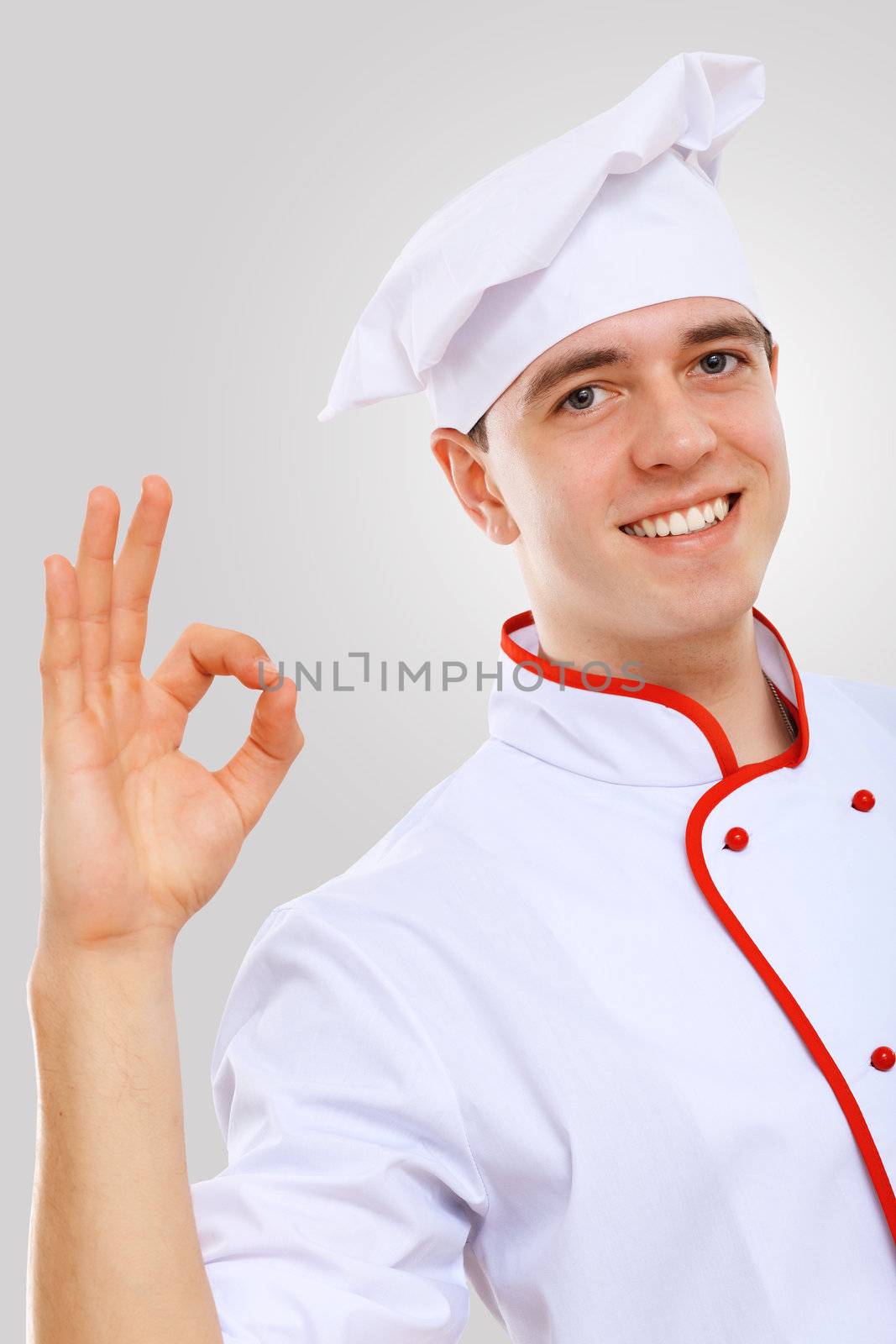 Young male chef in red apron against grey background