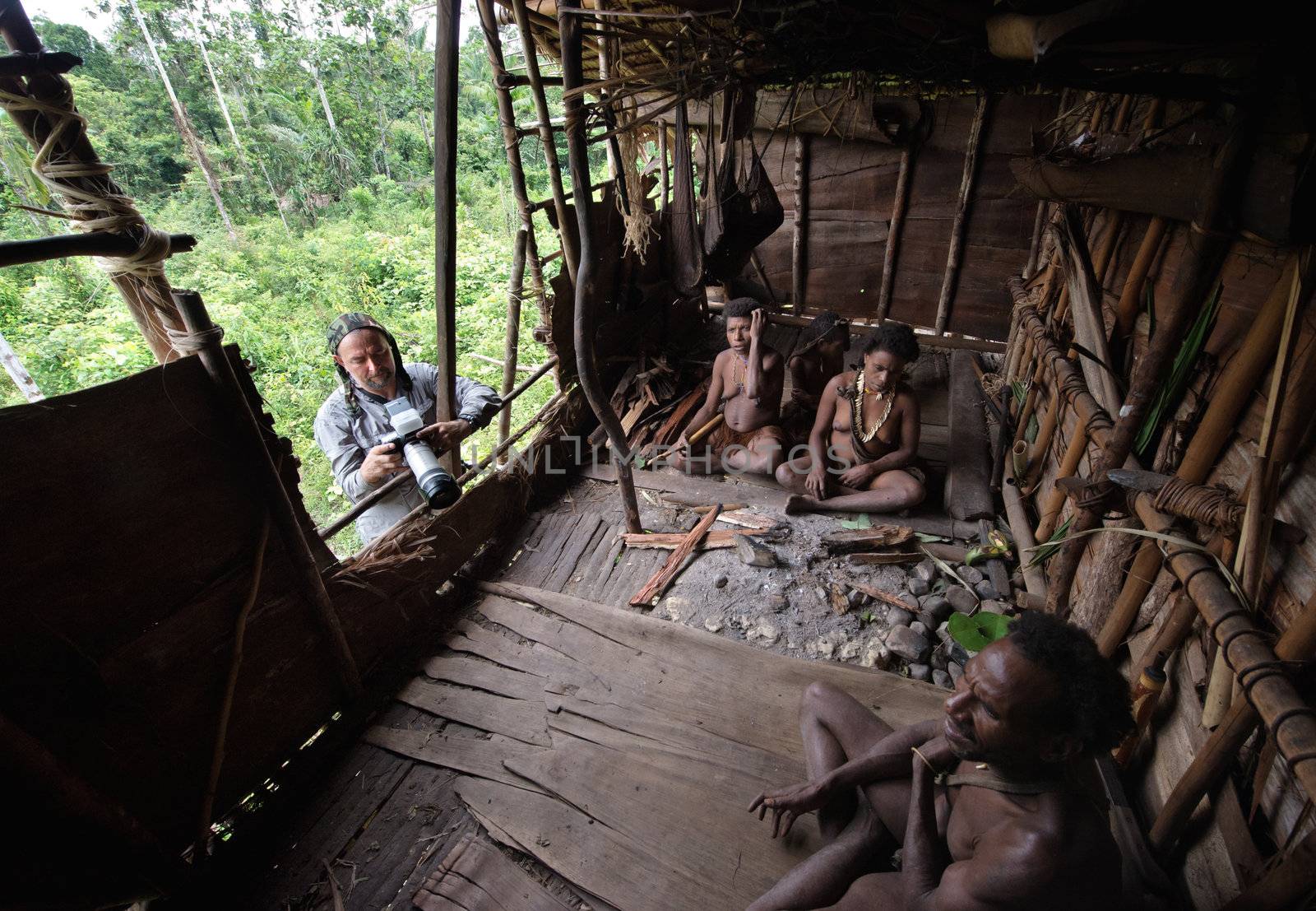 INDONESIA, NEW GUINEA, IRIAN JAYA, ONNI VILLAGE - JUNY 27: White man with camera and Korowai people in the traditional wooden house built on a tree. New Guinea Island, Indonesia. June 27 2012