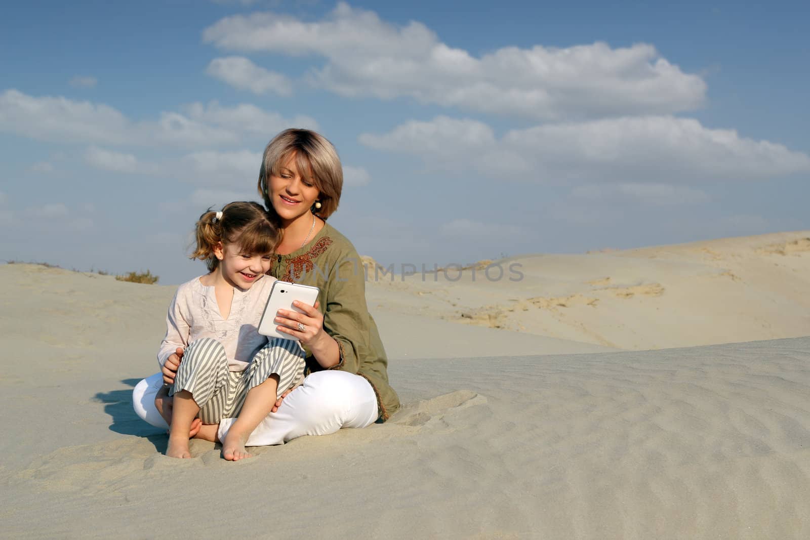 mother and daughter play with tablet in desert