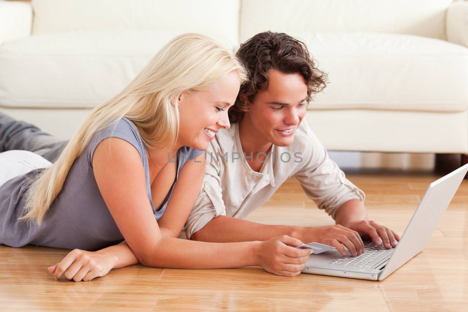 Young couple shopping online while lying on the floor