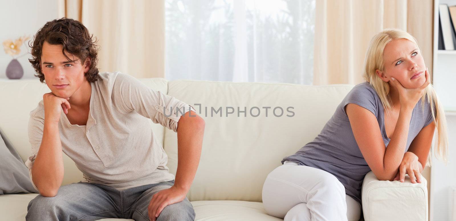 Upset young couple sitting on a couch with their hand on their chin