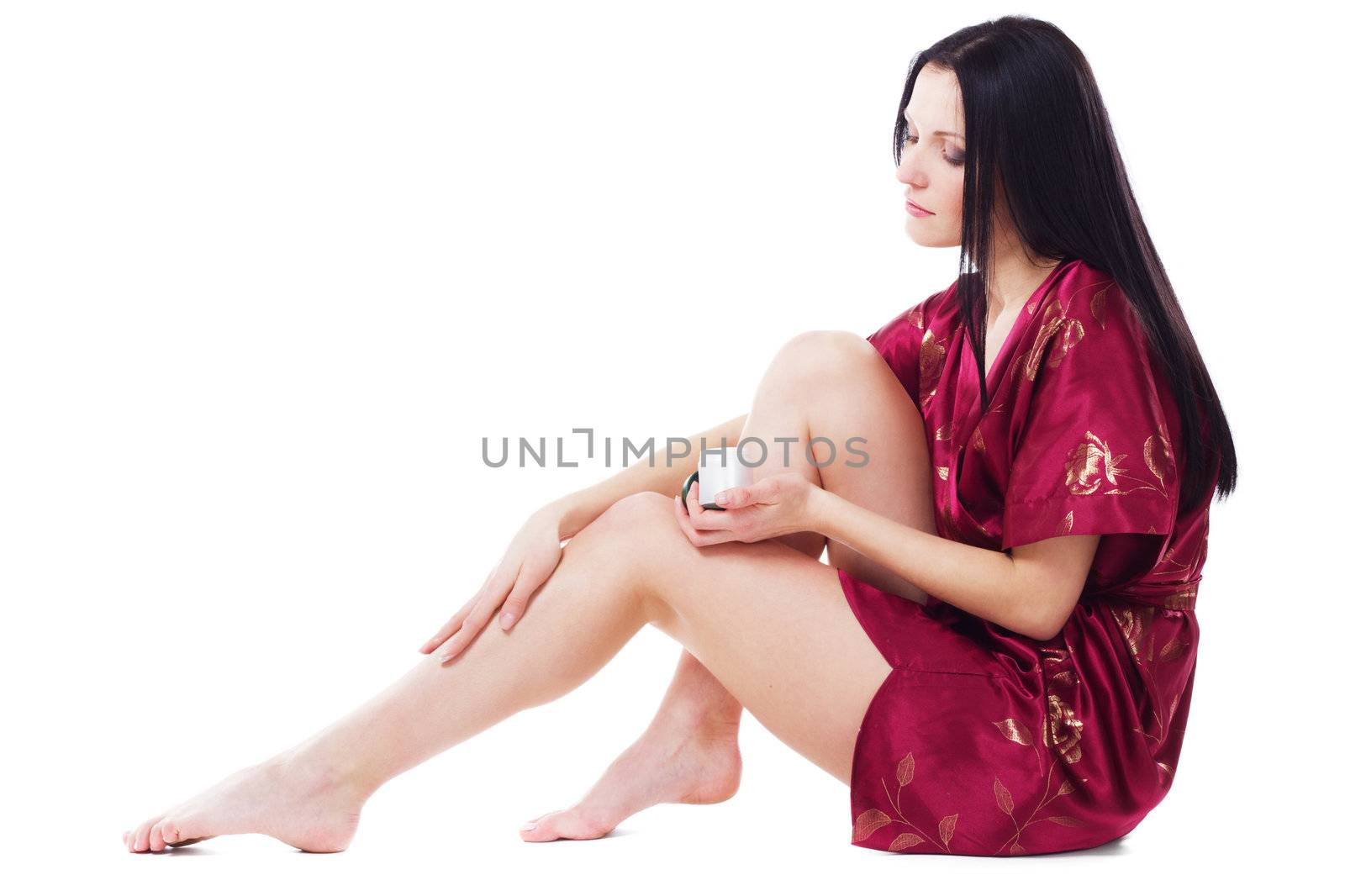 Beautiful woman applying body cream on her attractive legs, isolated on white 