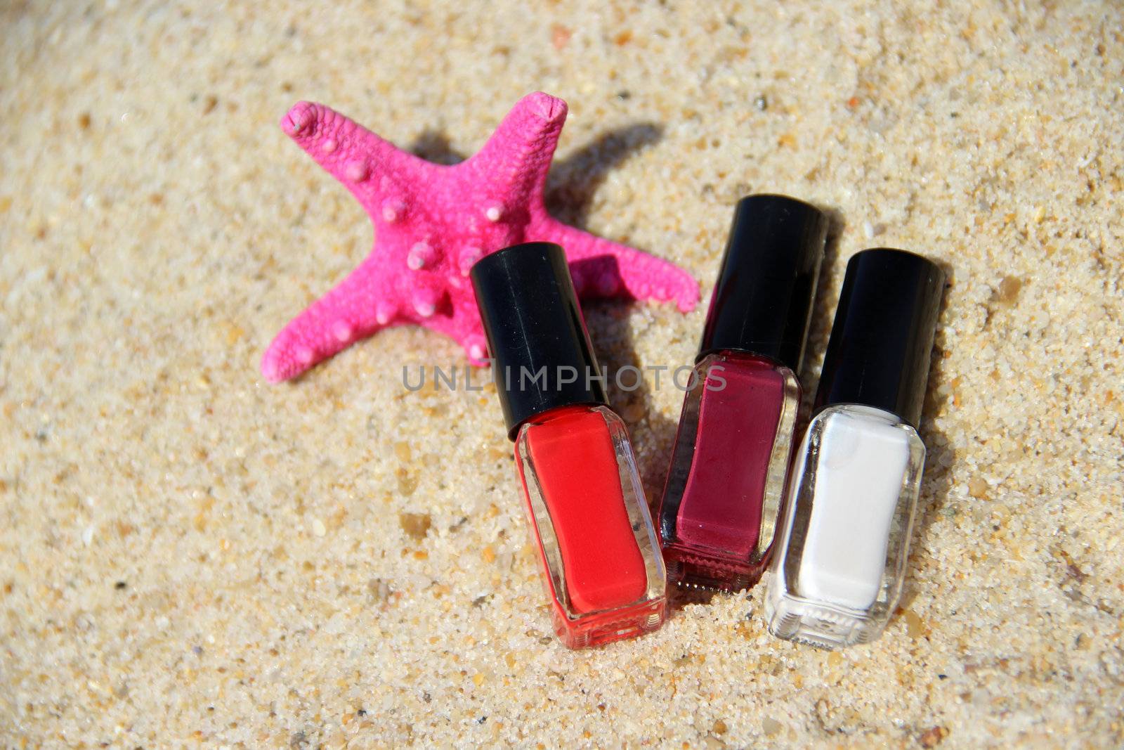 Three nail polish bottle on the beach and pink starfish;