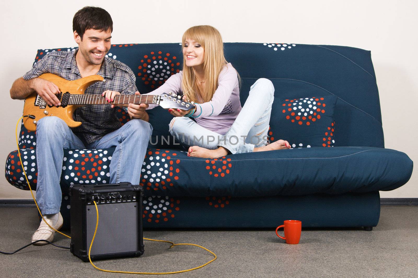 Young beautiful couple resting at home and playing electric guitar