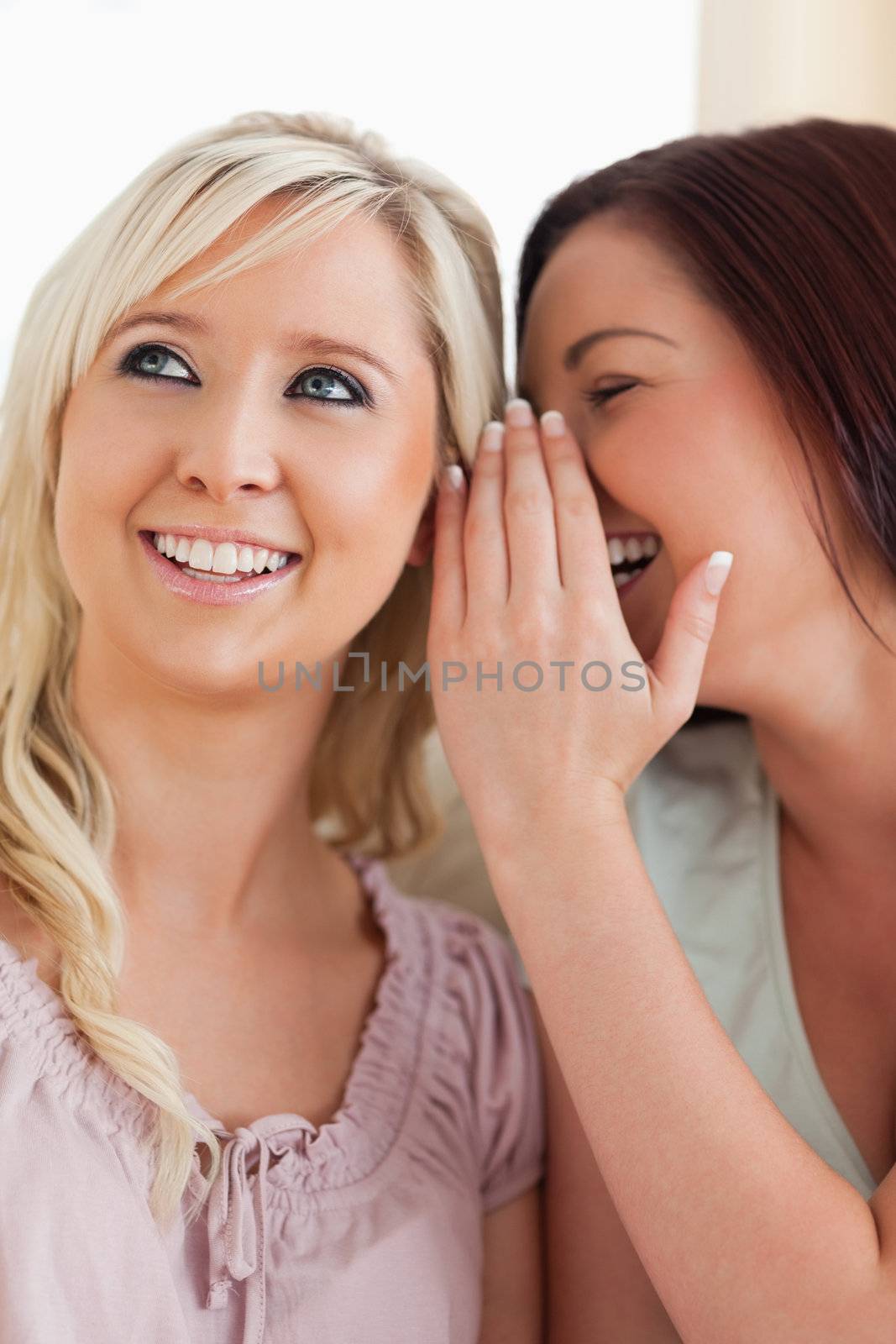 Smiling woman telling her friend a secret in a living room