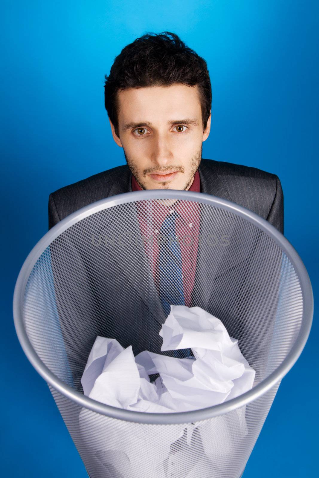 Young businessman playing baskteball with crumpled paper, blue background