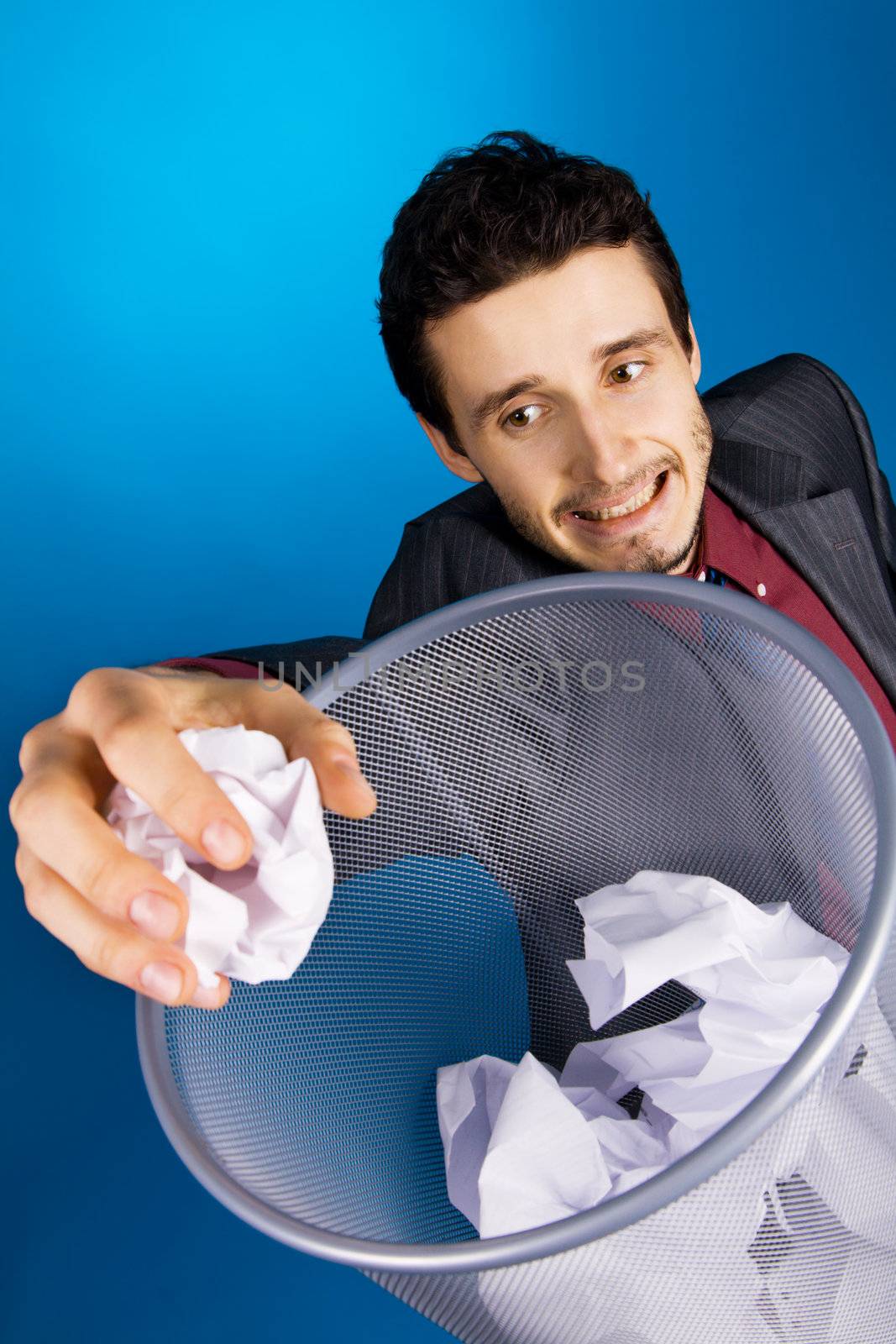 Young businessman playing baskteball with crumpled paper, blue background