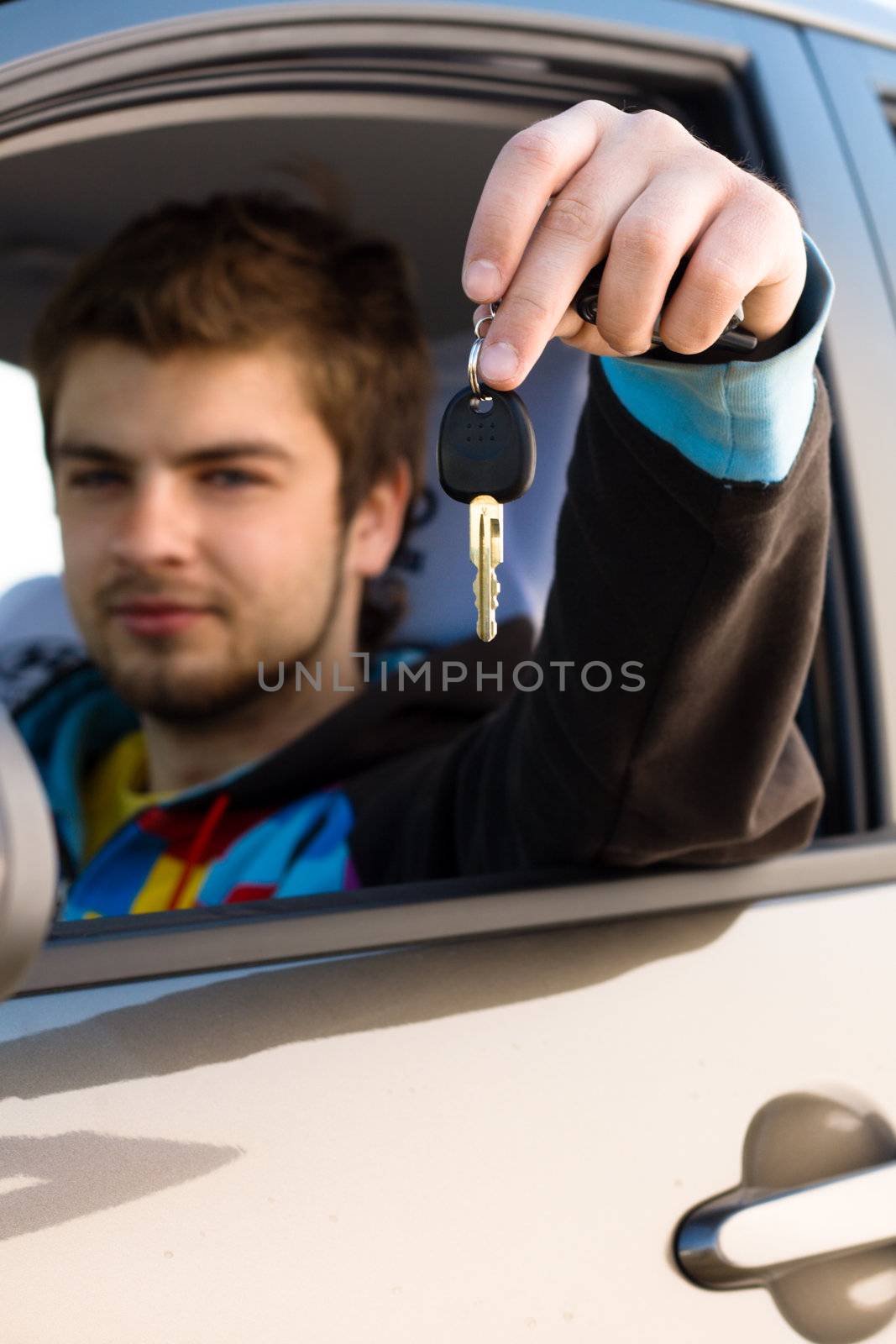Happy young man sitting ina new car holding out keys