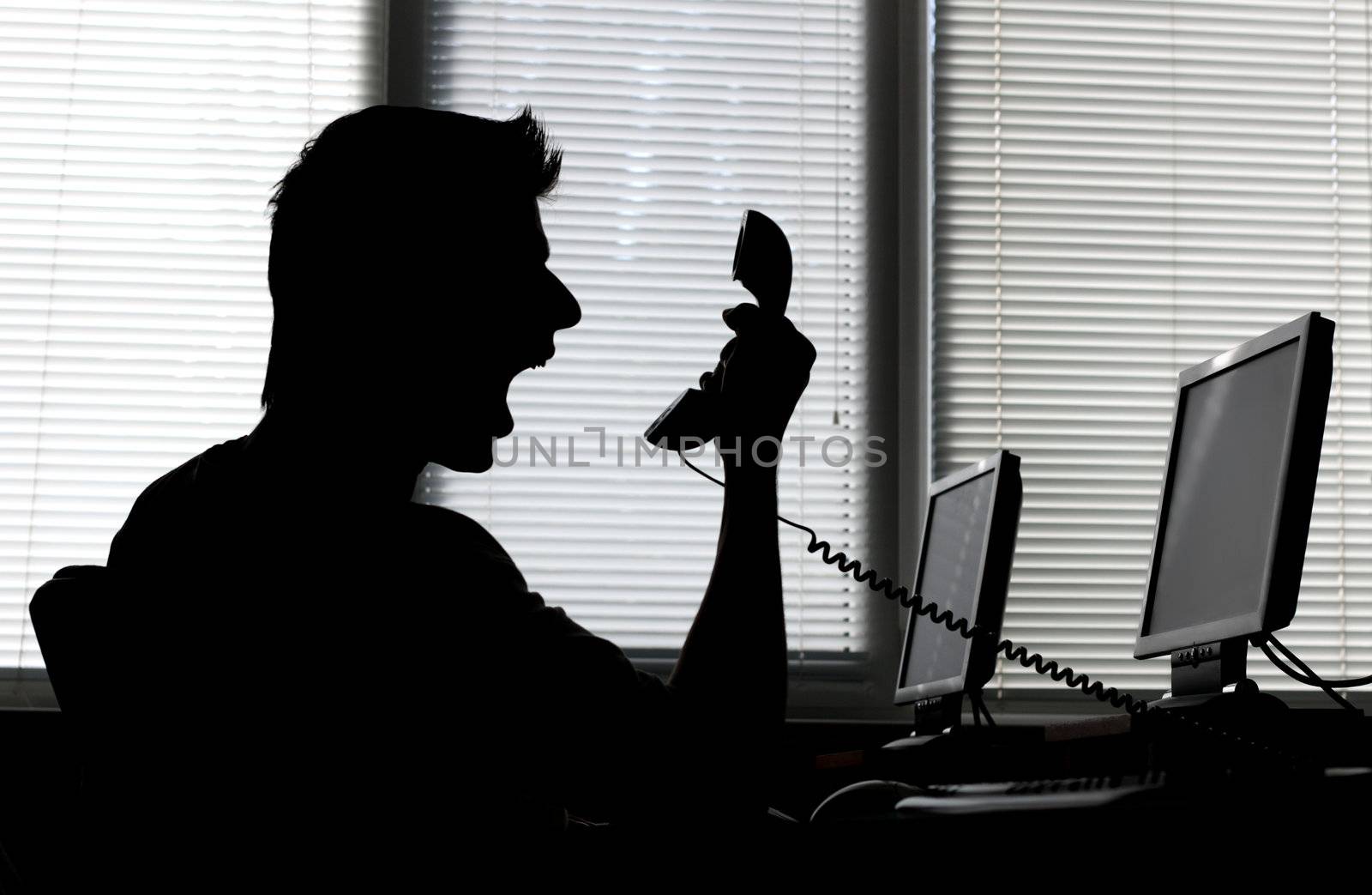 Silhouette of an angry man shouting into the phone receiver in his office