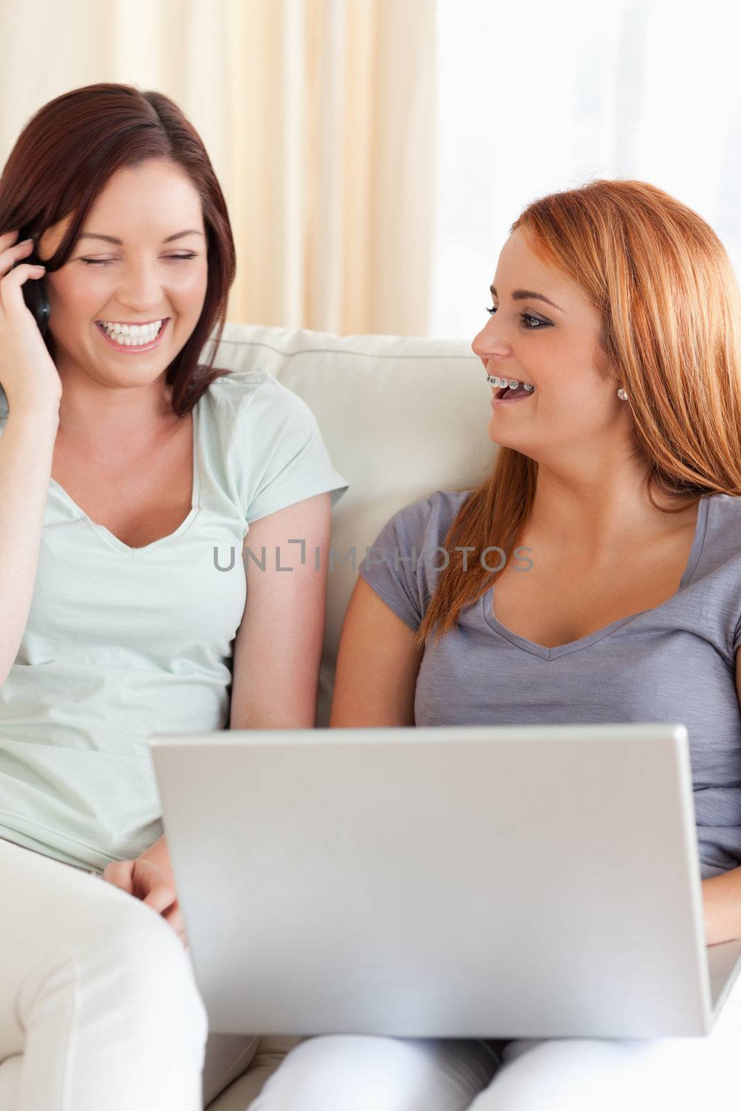 Laughing Women sitting on a sofa with a laptop and a phone in a living room