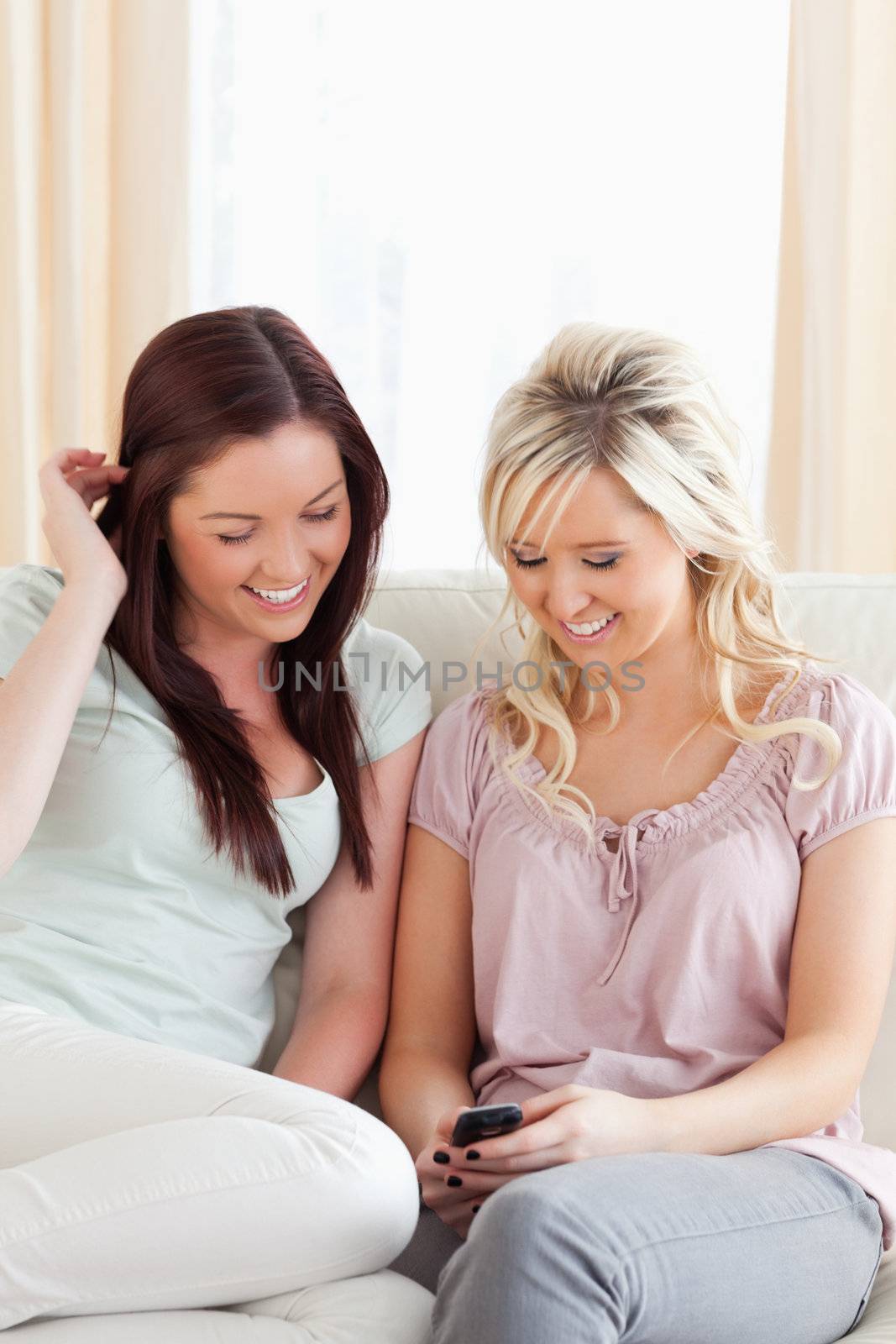 Young smiling Women sitting on a sofa with a phone by Wavebreakmedia