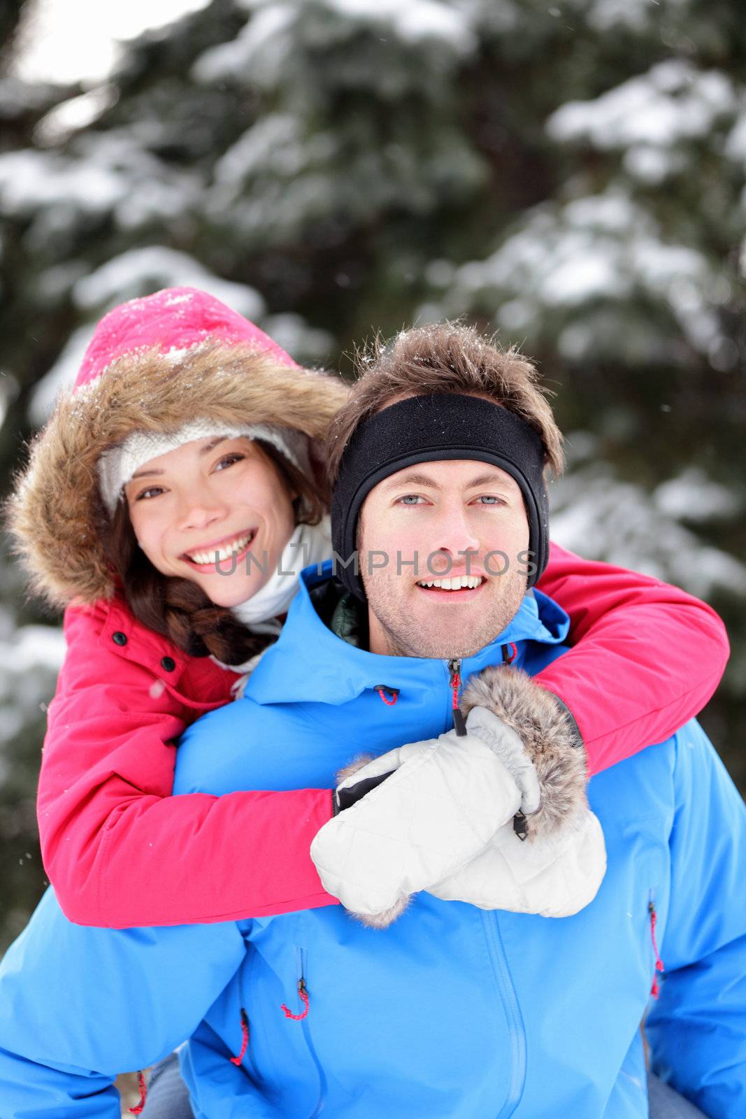 Happy young couple in winter having fun embracing having fun together in winter snow forest. Young interracial couple, Asian woman, Caucasian man.