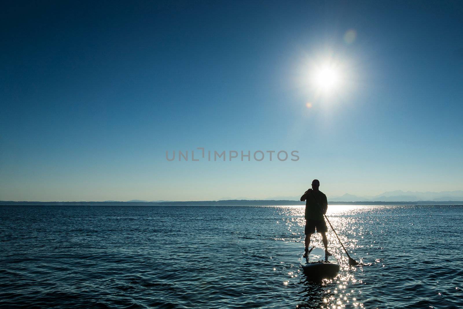 Man paddling stand up paddle board at sunset.