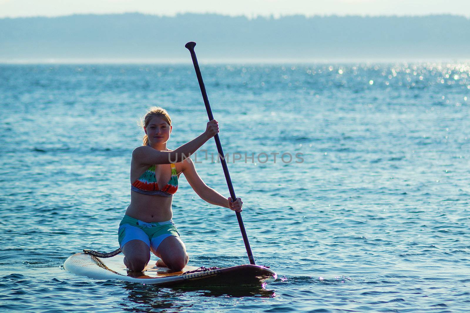 Woman paddling stand up paddle board while kneeling.