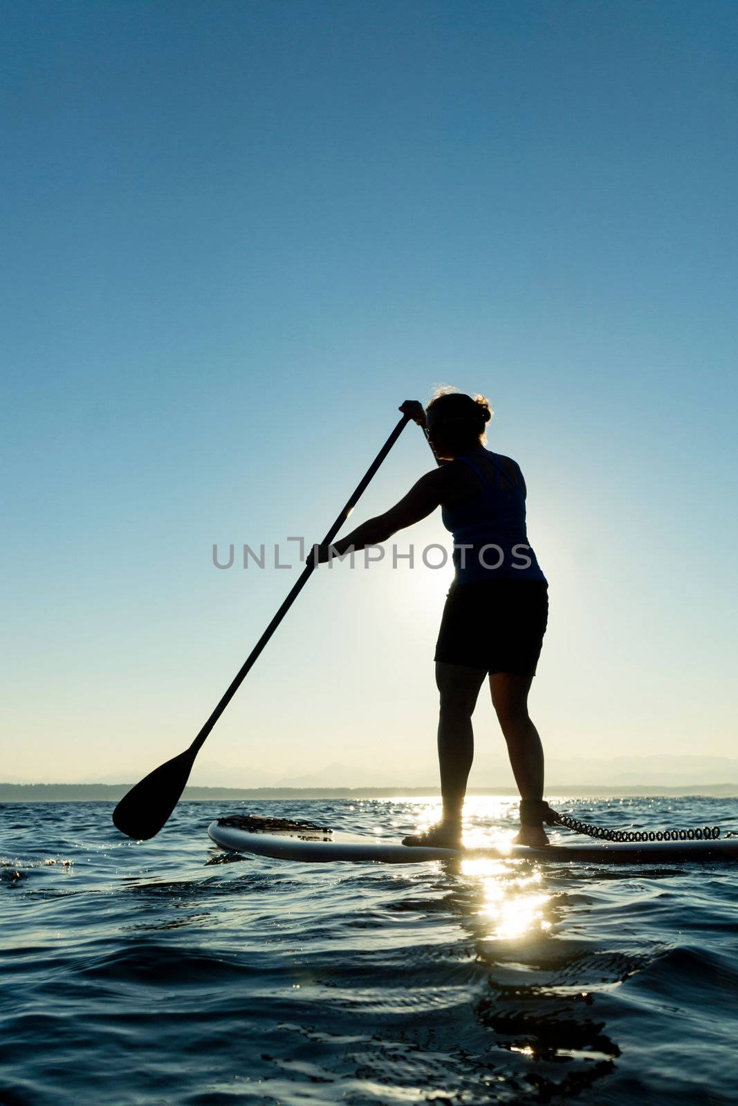 Womann paddling stand up paddle board at sunset with blue sky in background.