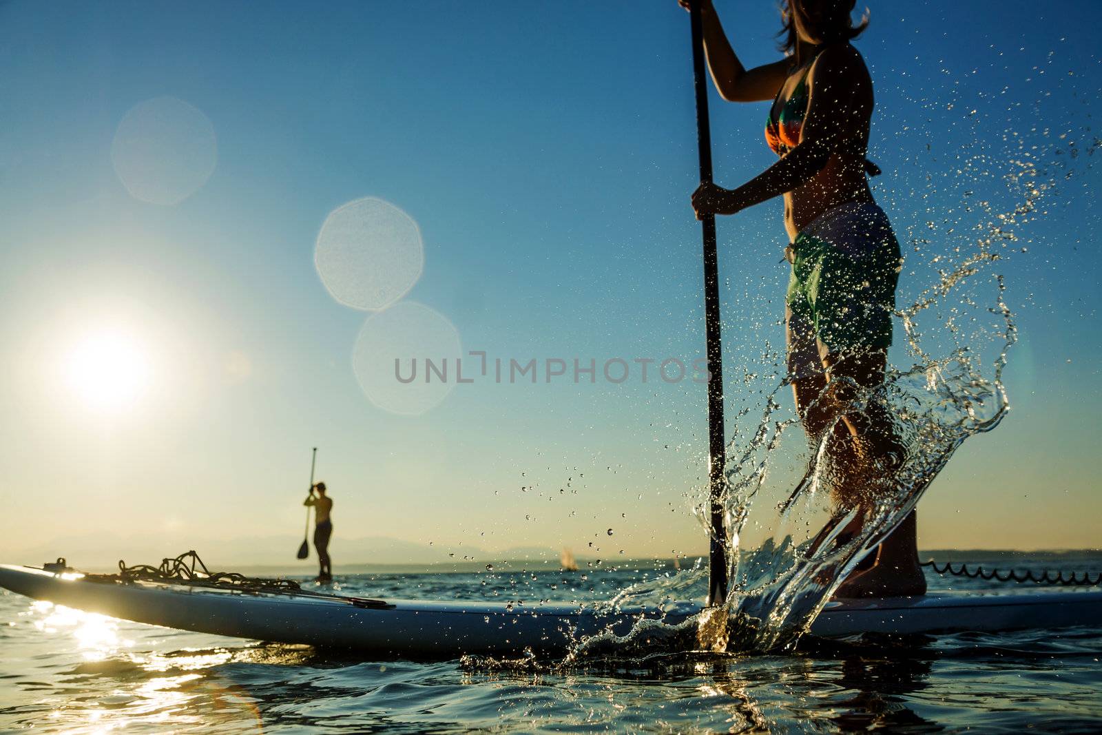 Woman paddling stand up paddle board at sunset with splash in foreground.