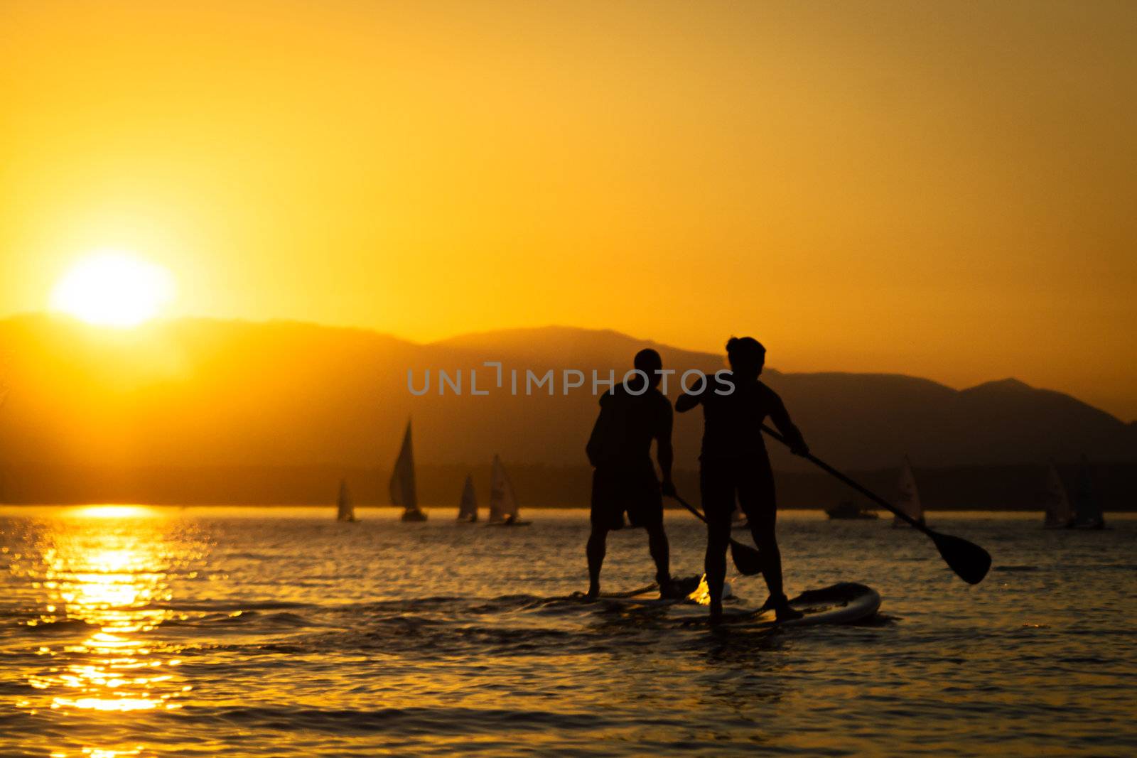 Couple paddling stand up paddle boards at sunset with mountains in background.