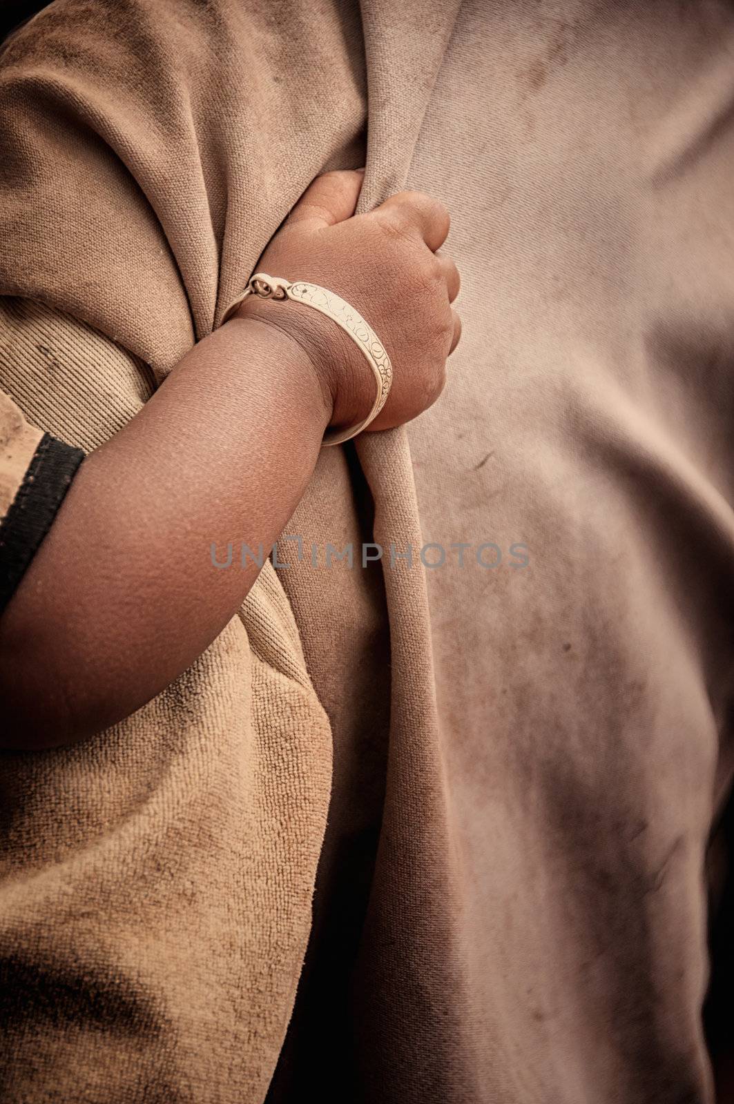 Poor child's hand holding on to a man, detail of the arm with a bracelet