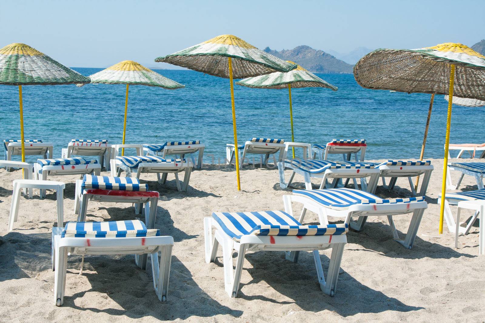 Sun loungers and wicker parasols on sandy beach in Turgutreis in the Bodrum Peninsula, Turkey.