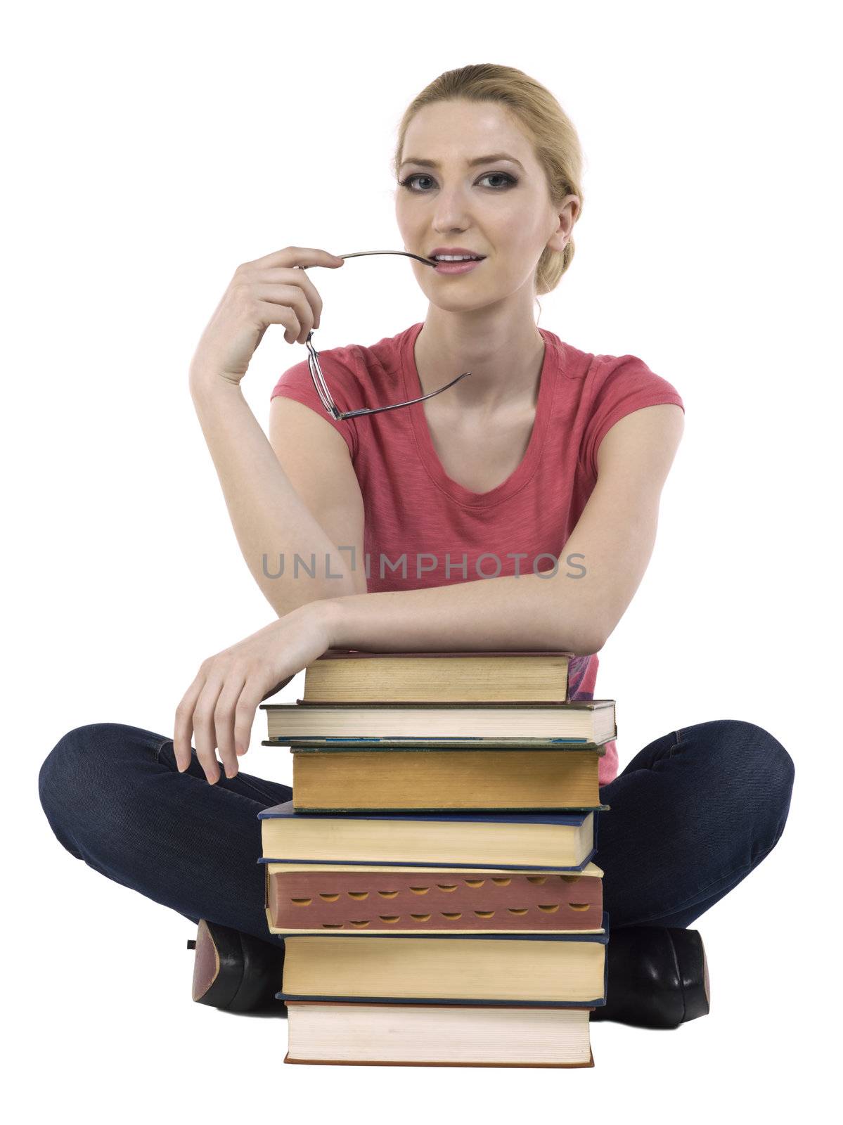 Female student biting her eye glasses while sitting with a pile of books