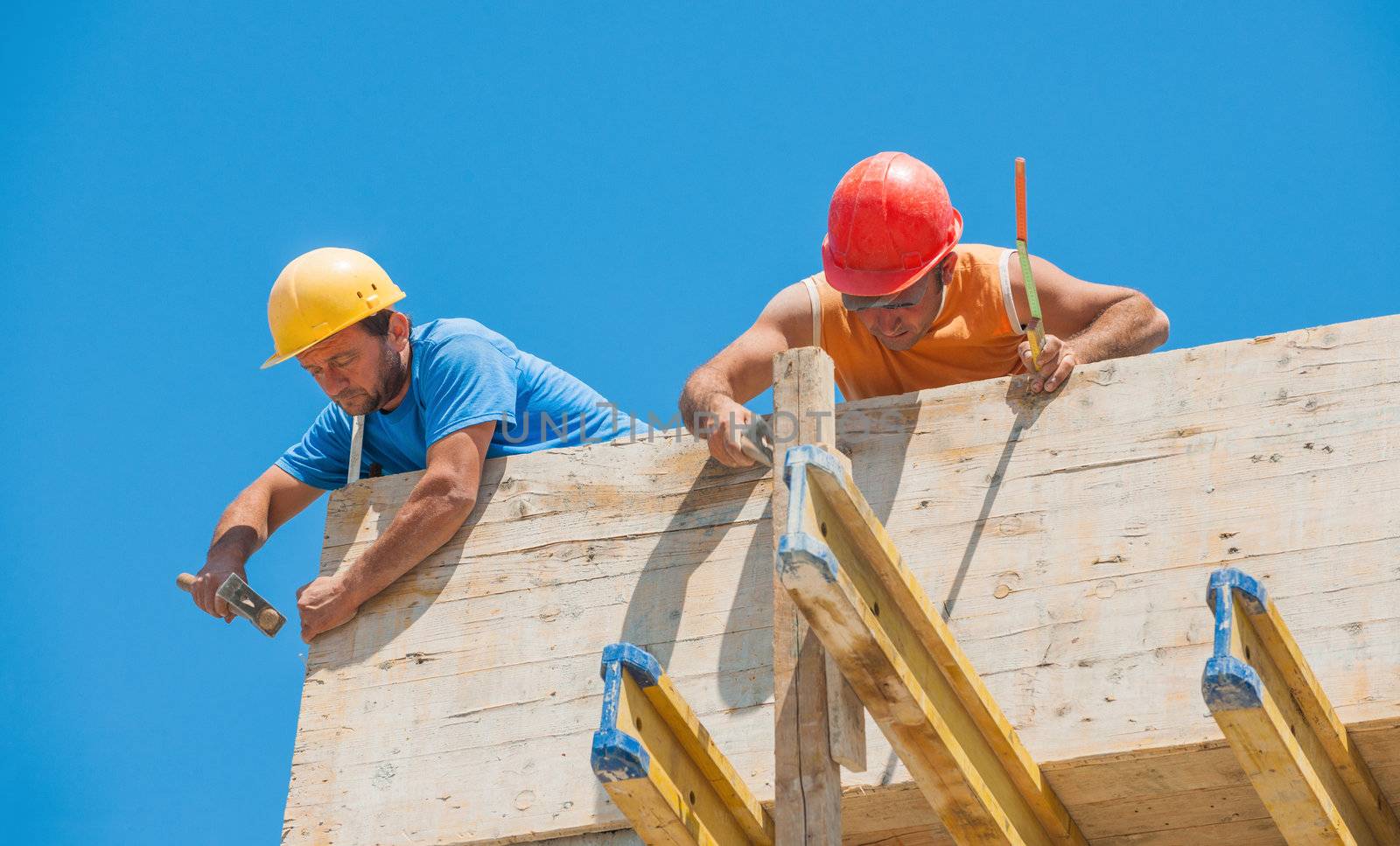 Construction workers nailing cement formwork in place by akarelias