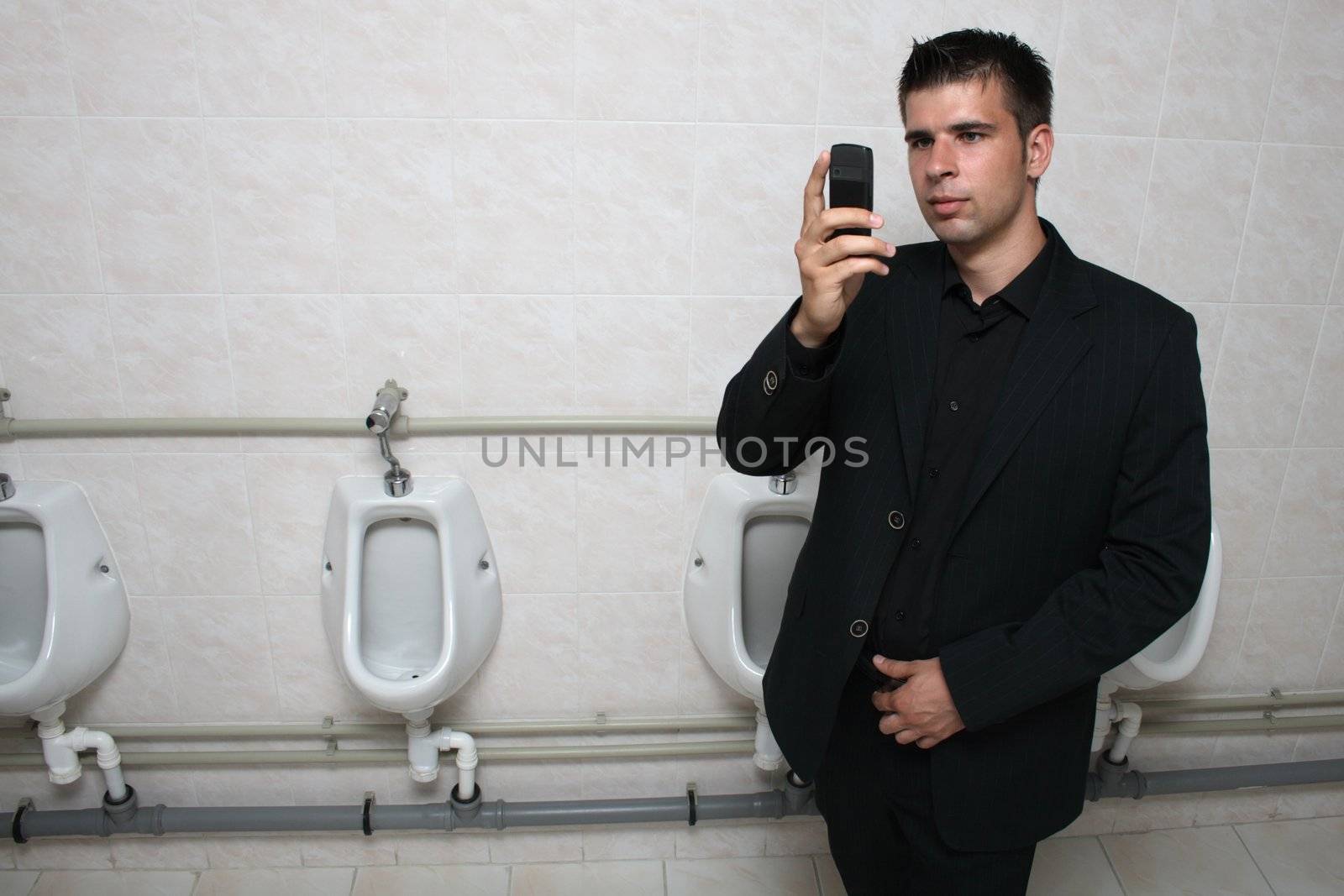 Businessman holding his mobile phone in a toilet, taking picture of himself.
