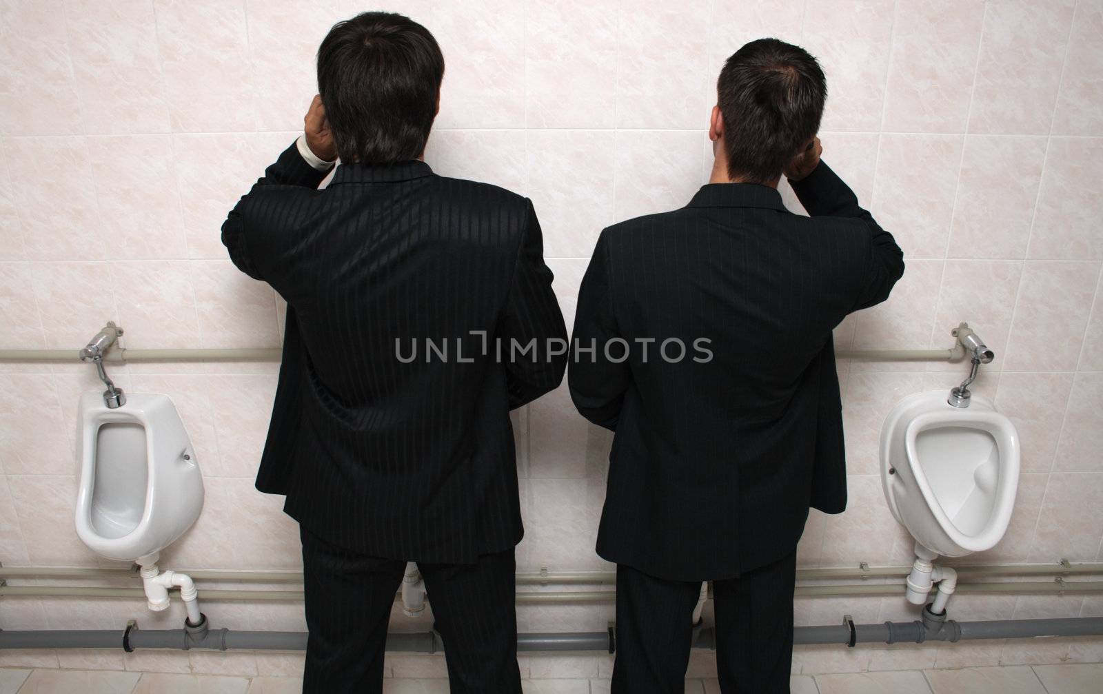 Two businessman talking by mobile phones in a WC