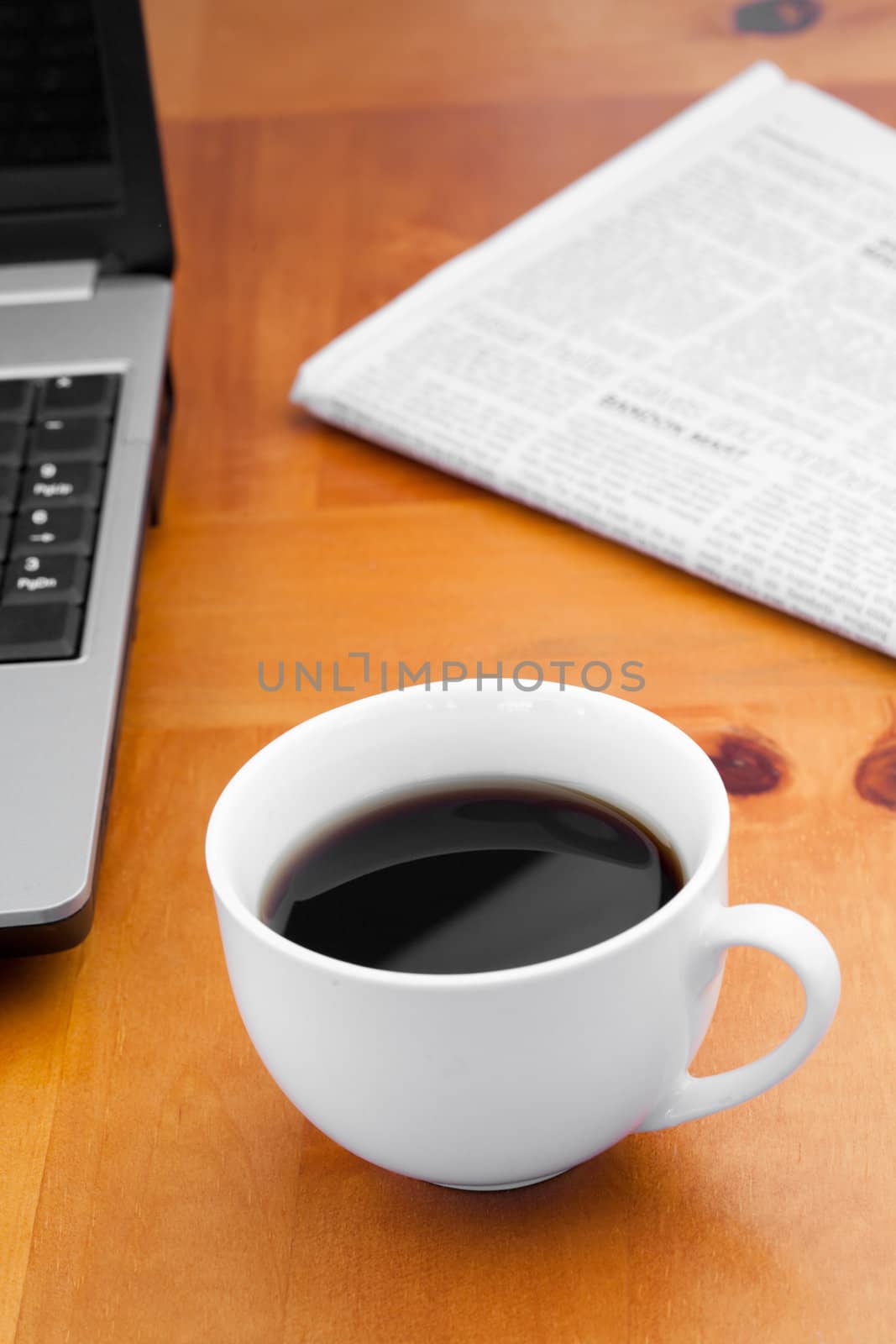 White cup of coffee with laptop and newspaper on a desk