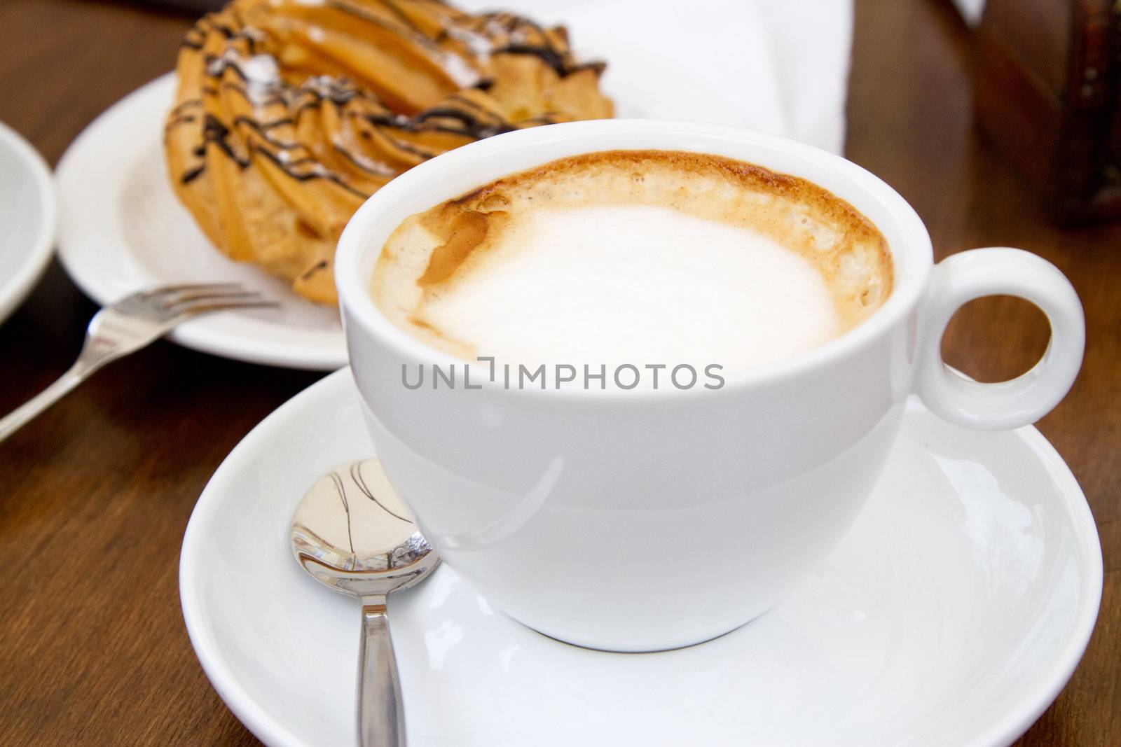 Cup of coffee on wooden table with cake on background