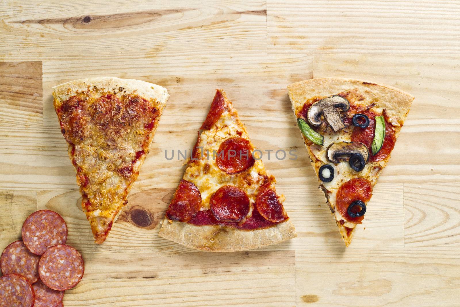 Top view of three baked pizza pie with slices of ham over wooden surface