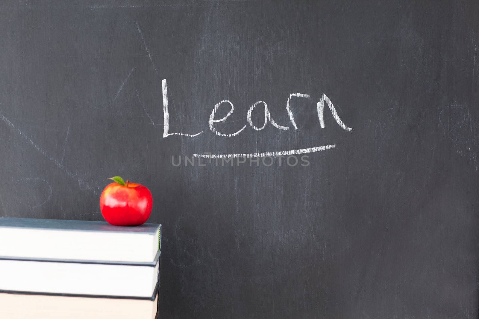 Stack of books with a red apple and a blackboard with "learn" written on it