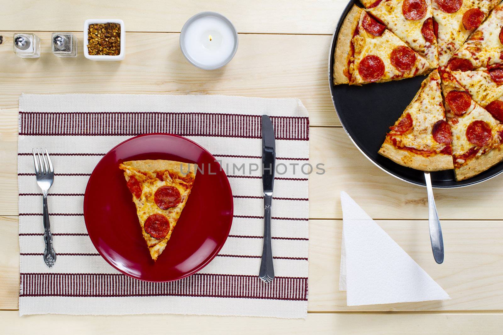 Slice of pizza on plate with pizza on pan on wooden board