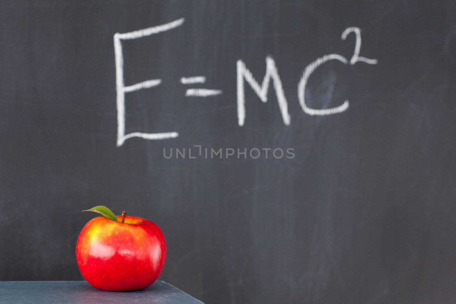 Stack of books with a red apple and a blackboard with a formula written on it