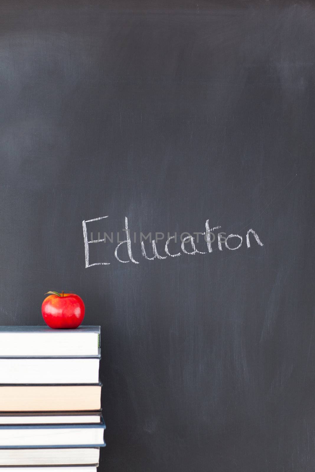 Stack of books with a red apple and a blackboard with "education" written on it