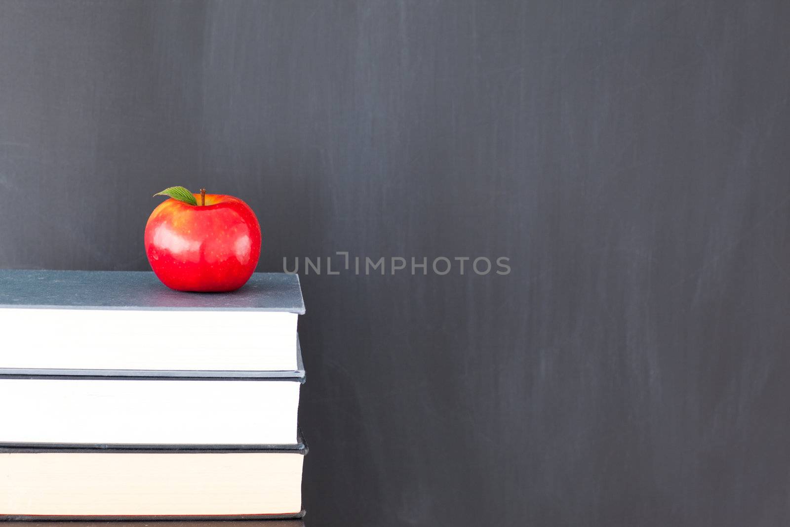 Stack of books with a red apple and a clean blackboard