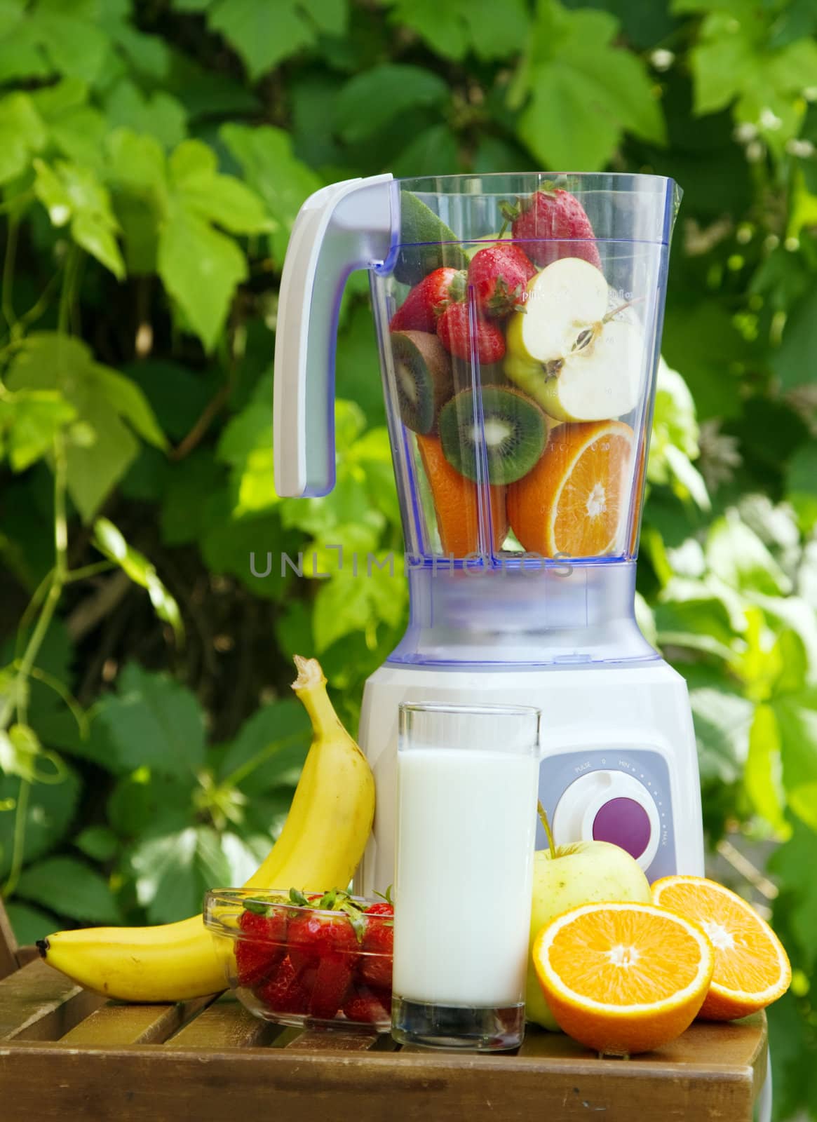 Electric blender with fruits in it, green leaves background