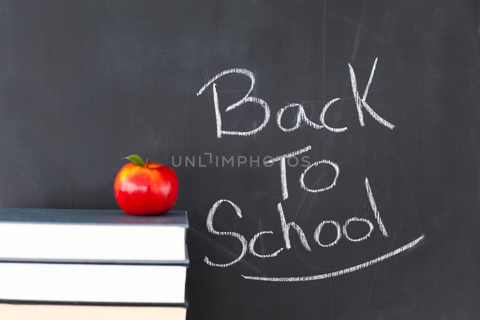 Stack of books with a red apple and a blackboard with "back to school" written on it