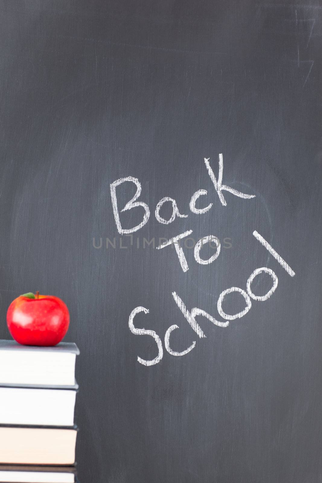 Stack of books with a red apple and a blackboard with "back to school" written on it