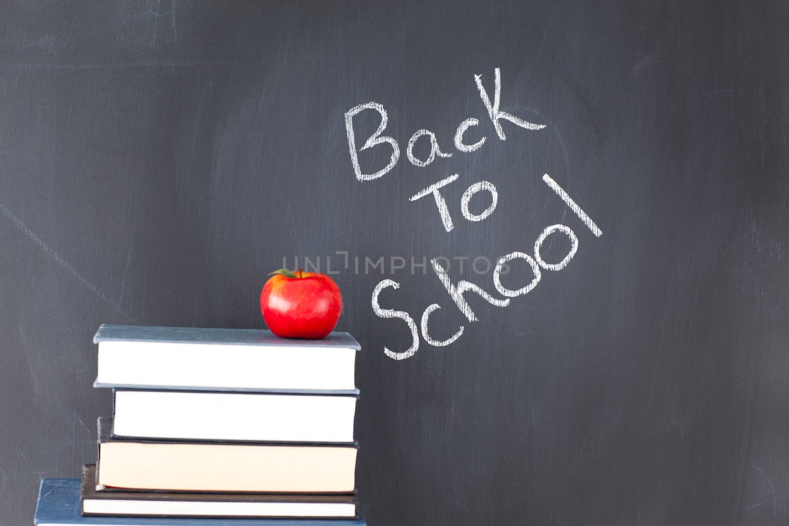 Stack of books with a red apple and a blackboard with "back to school" written on it