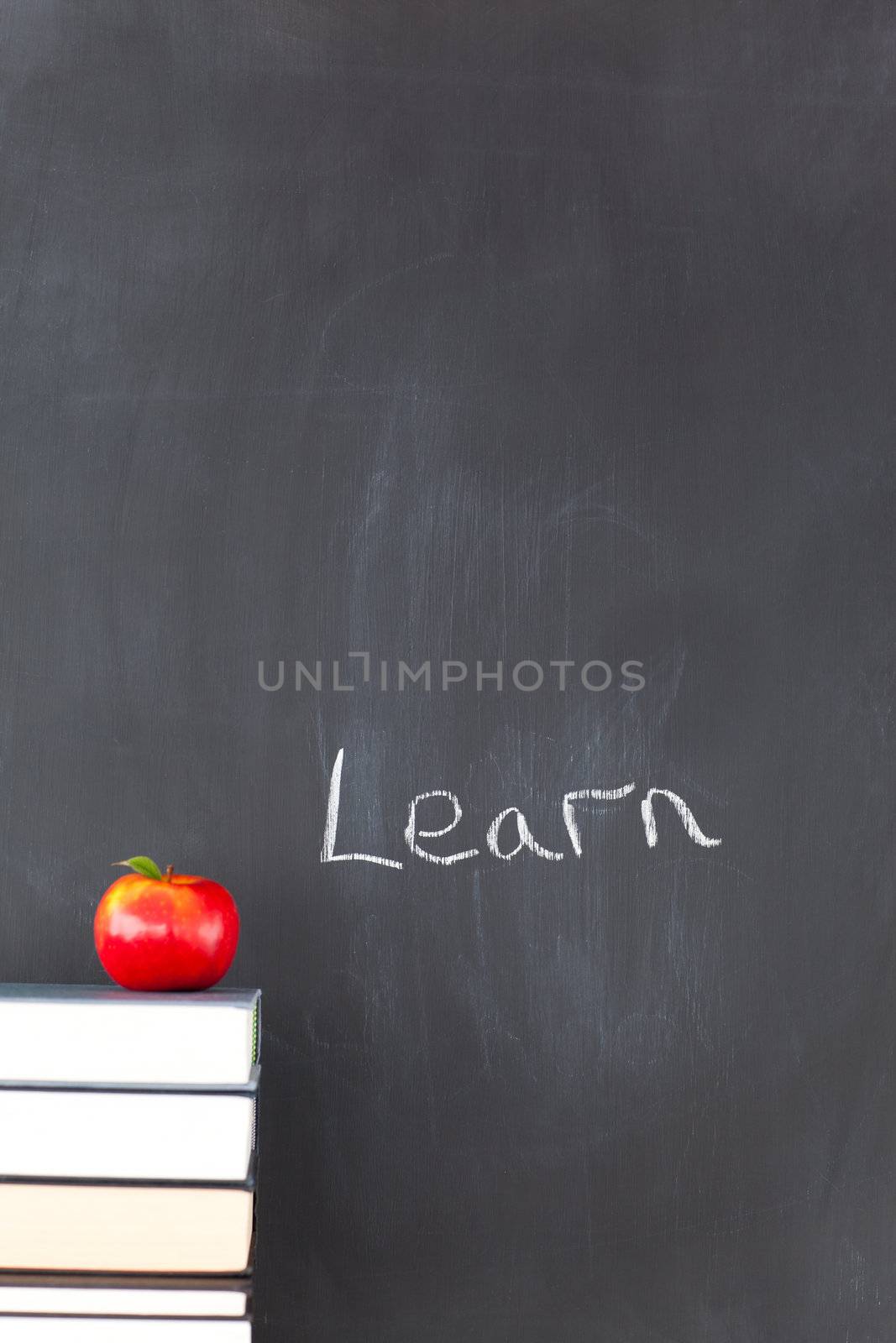 Stack of books with a red apple and a blackboard with "learn" written on it