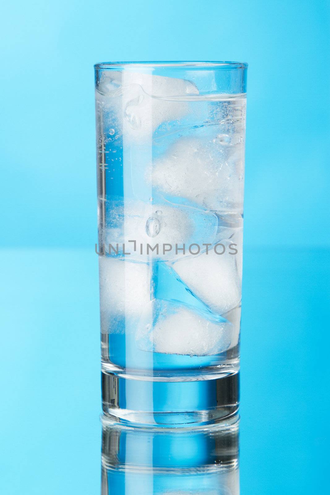 Glass of ice water on blue background, studio photo