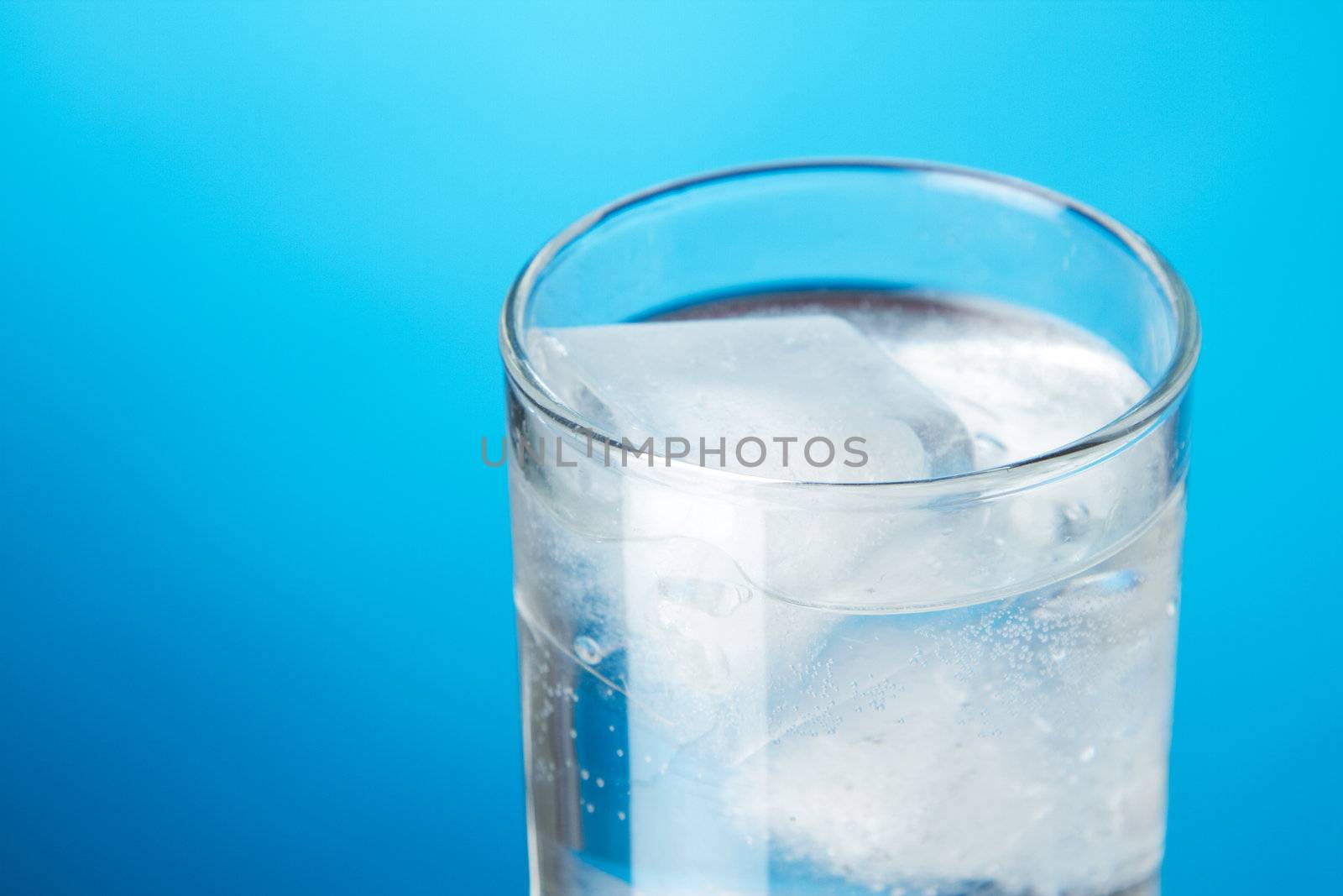 Glass of ice water on blue background, studio photo