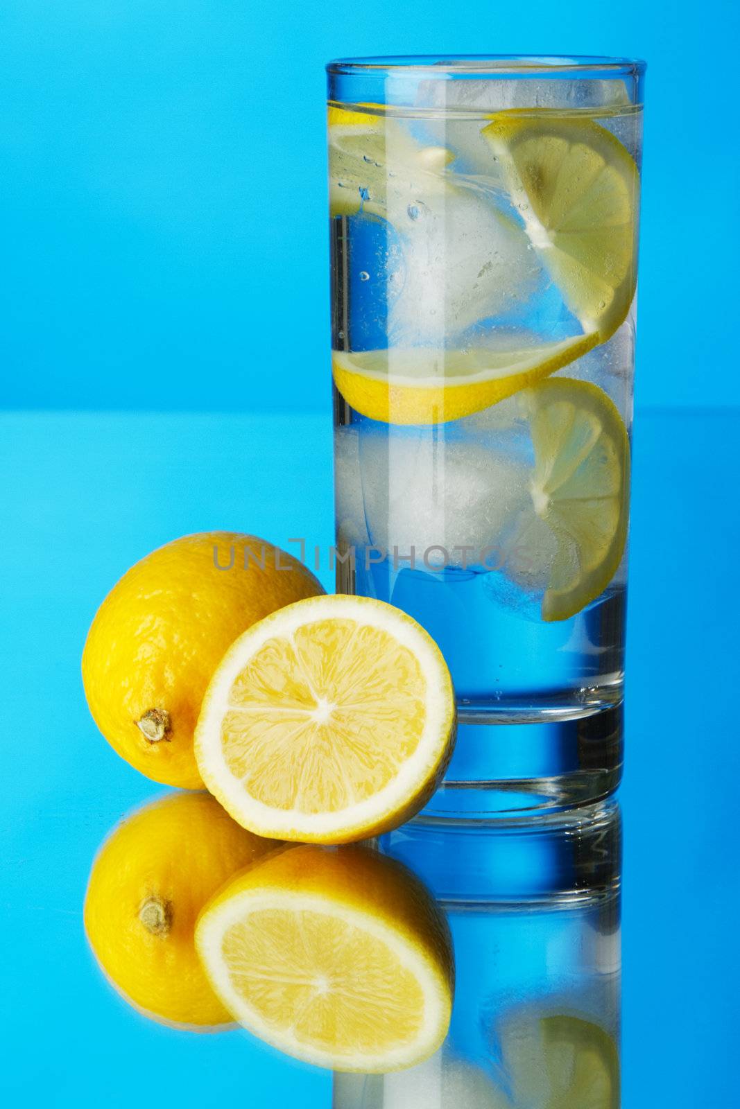 Glass of lemon ice water on blue background, studio photo