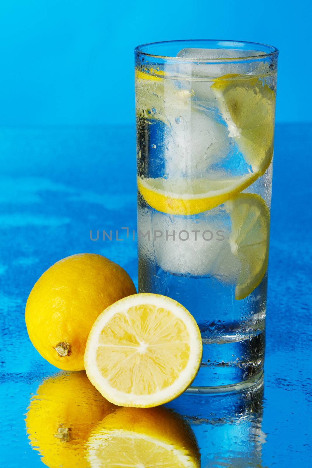 Glass of lemon ice water on blue background by Gdolgikh