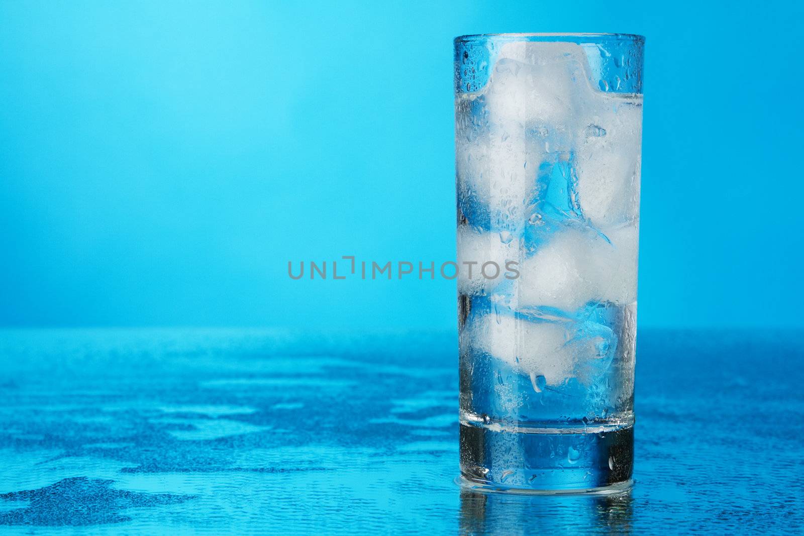 Glass of ice water on blue background, studio photo