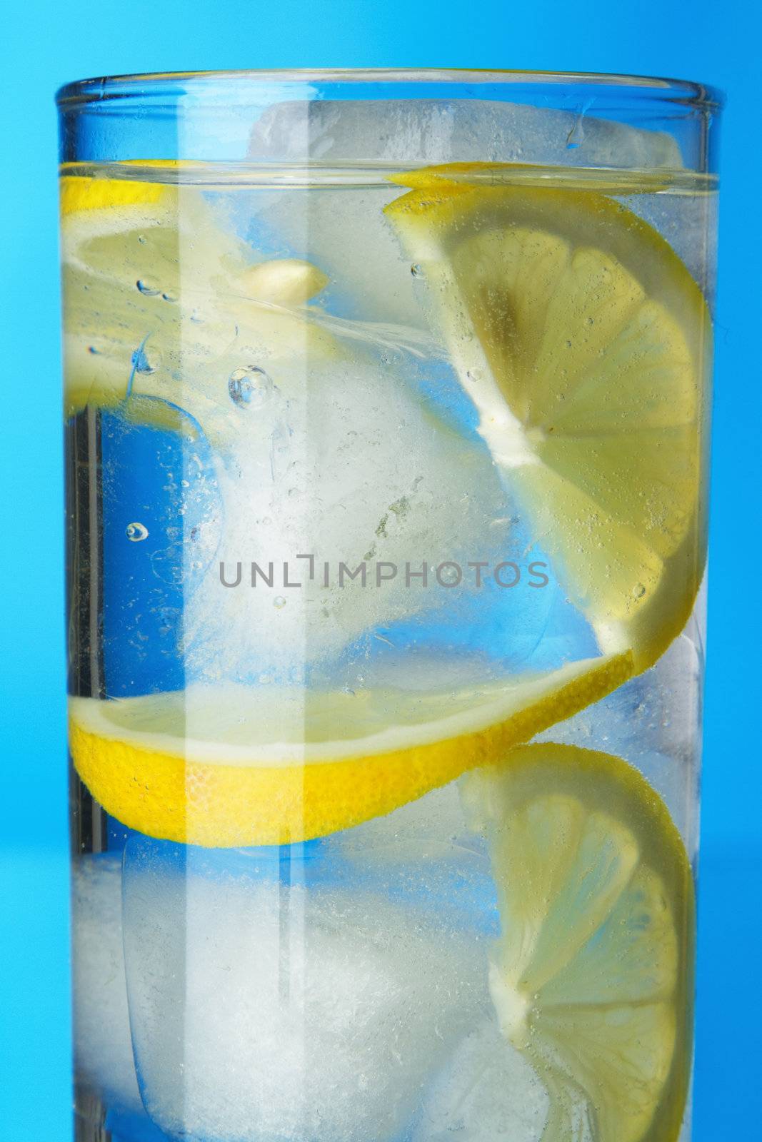 Glass of lemon ice water on blue background, studio photo